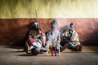 Three men sitting on the floor of a traditional dwelling in Eastern cape behind four lit candles