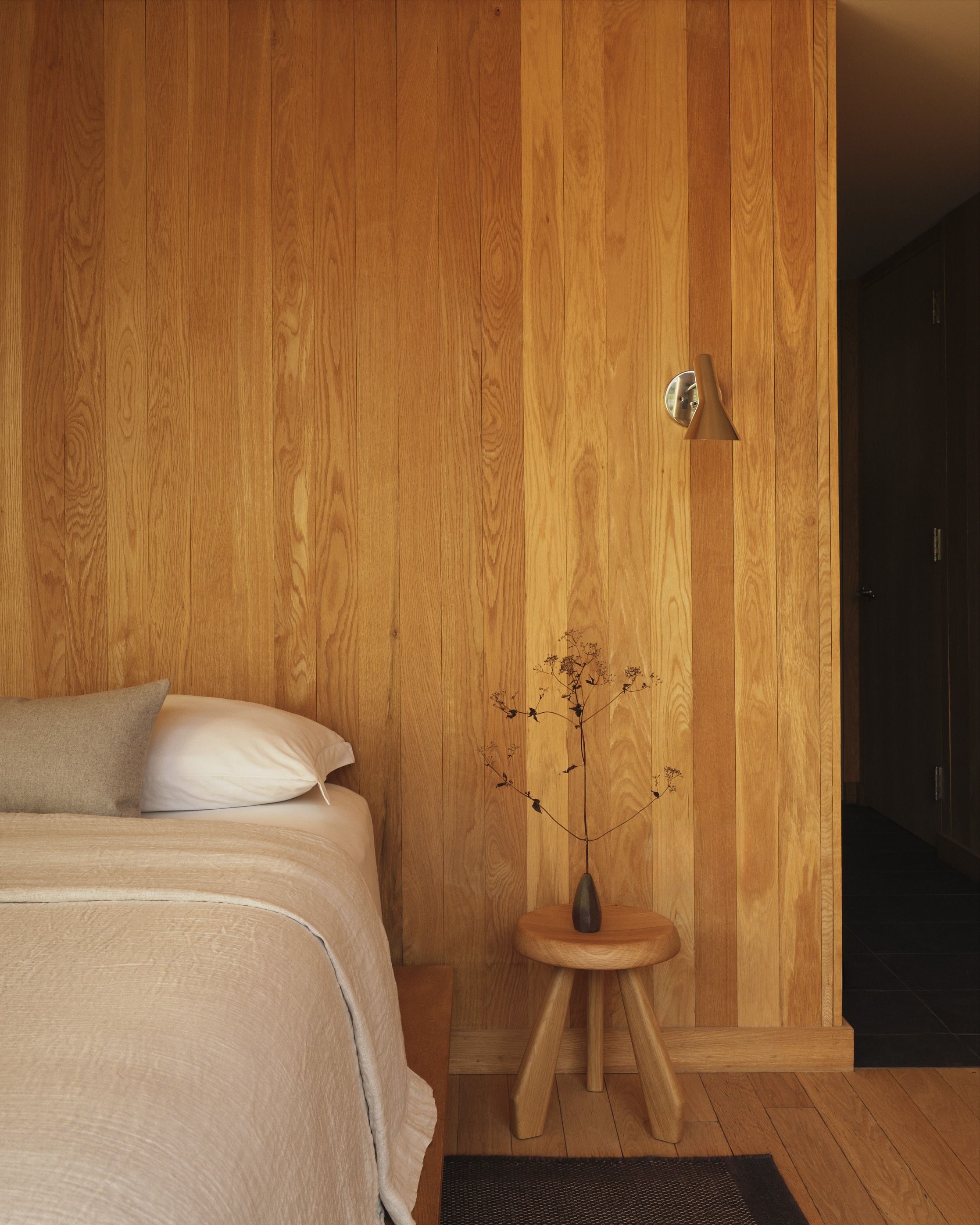A bed against a wood-clad wall with a stool as a bedside table.