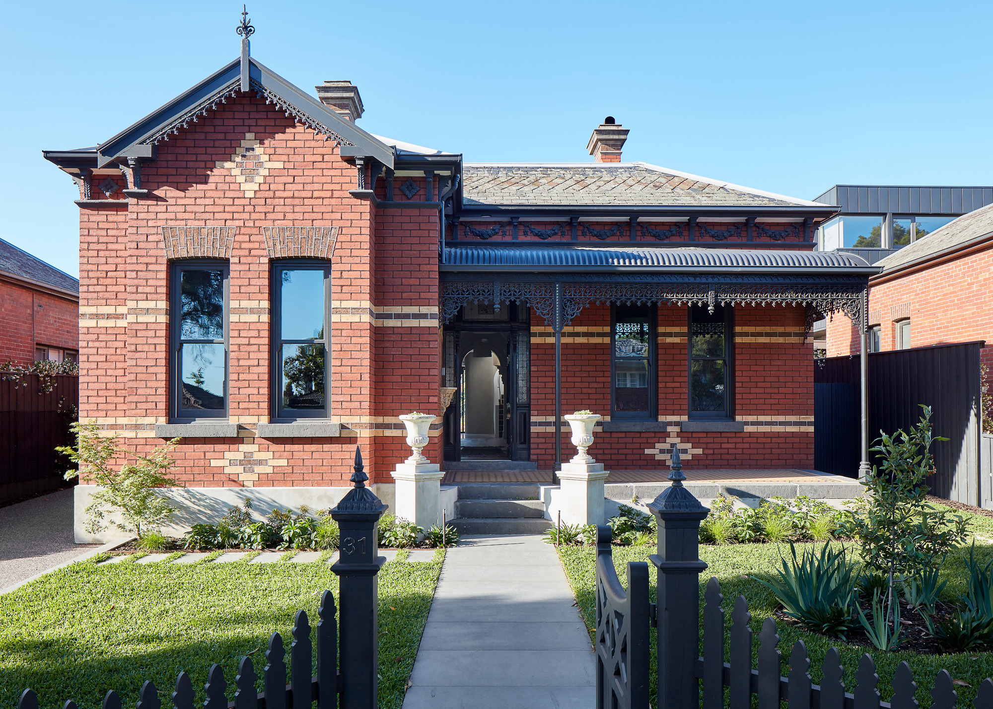 Victorian home with red brick exterior, ironwork canopy and grey slab pathway