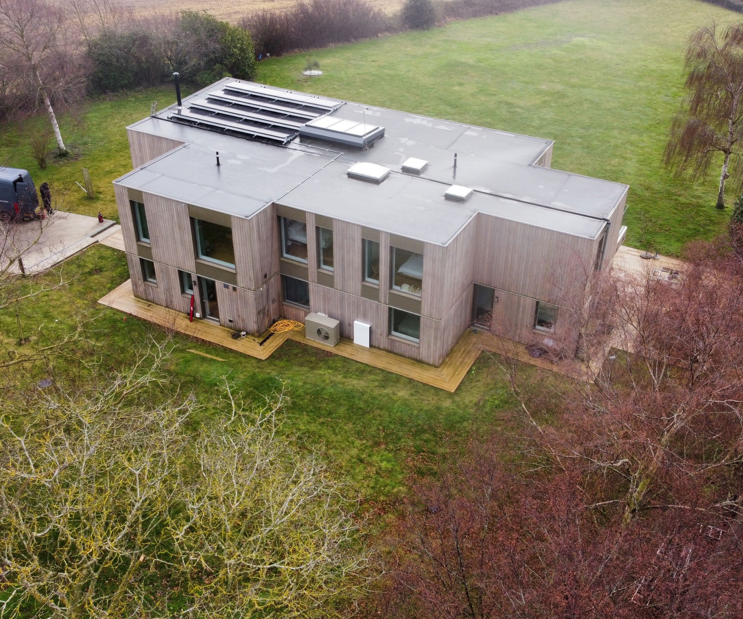 Modern timber-clad home with solar panels, showing a heat pump and Tesla Powerwall installed outside on the garden decking.