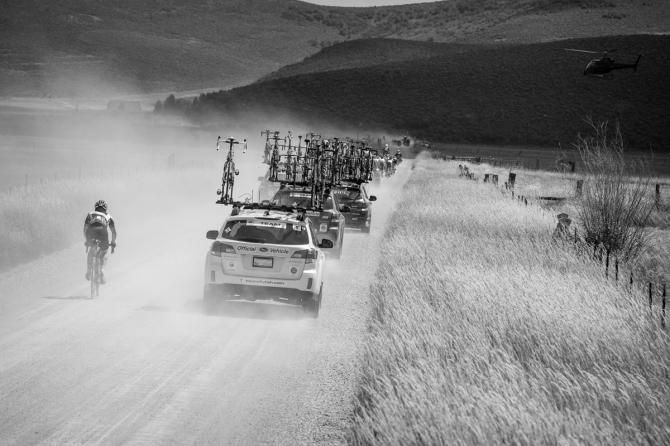 Team cars kick up dust as they pass by.