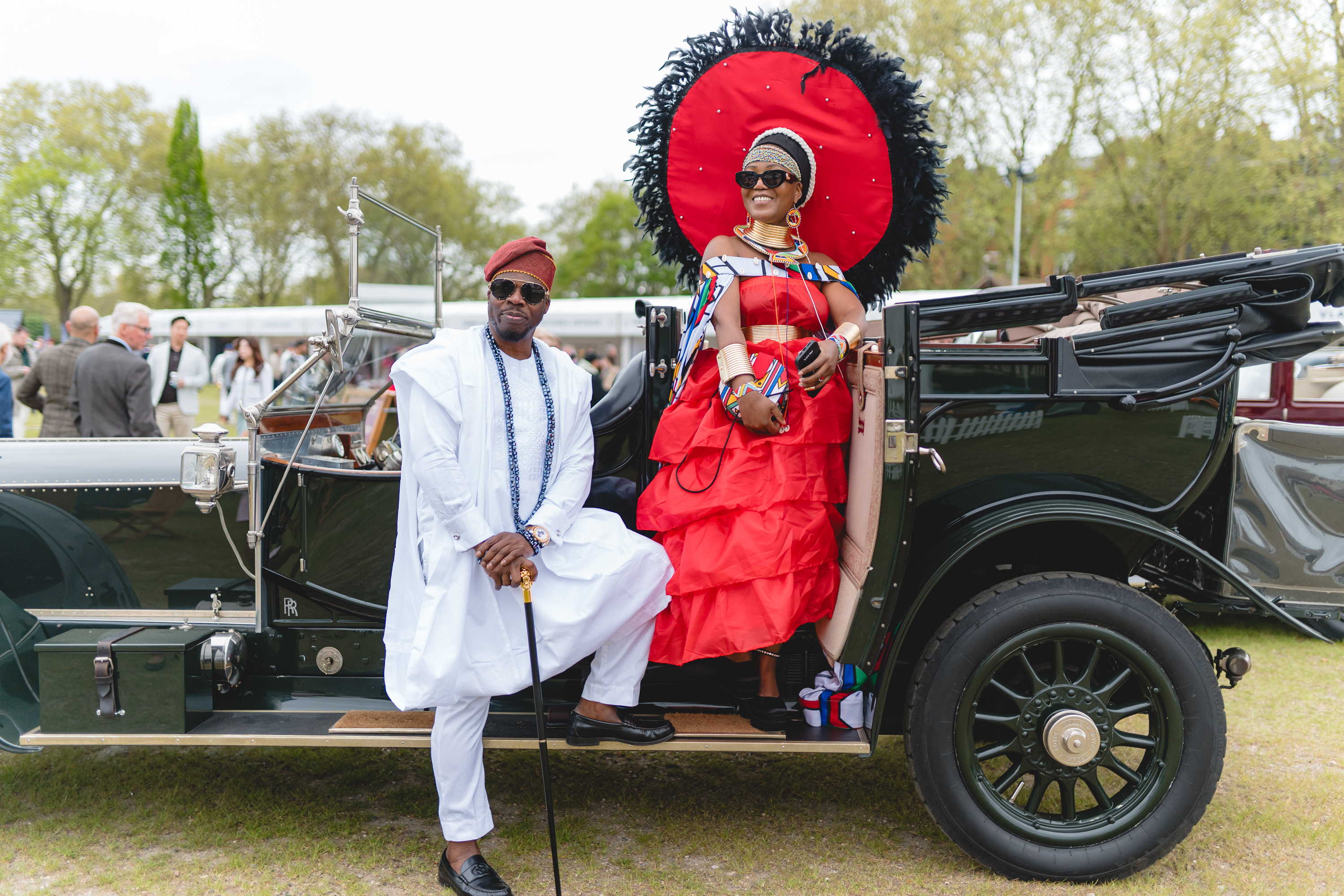A man and woman in traditional african dress atop a vintage car