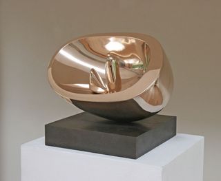 A rose gold, metallic sculpture, oval in shape with two other shapes inside