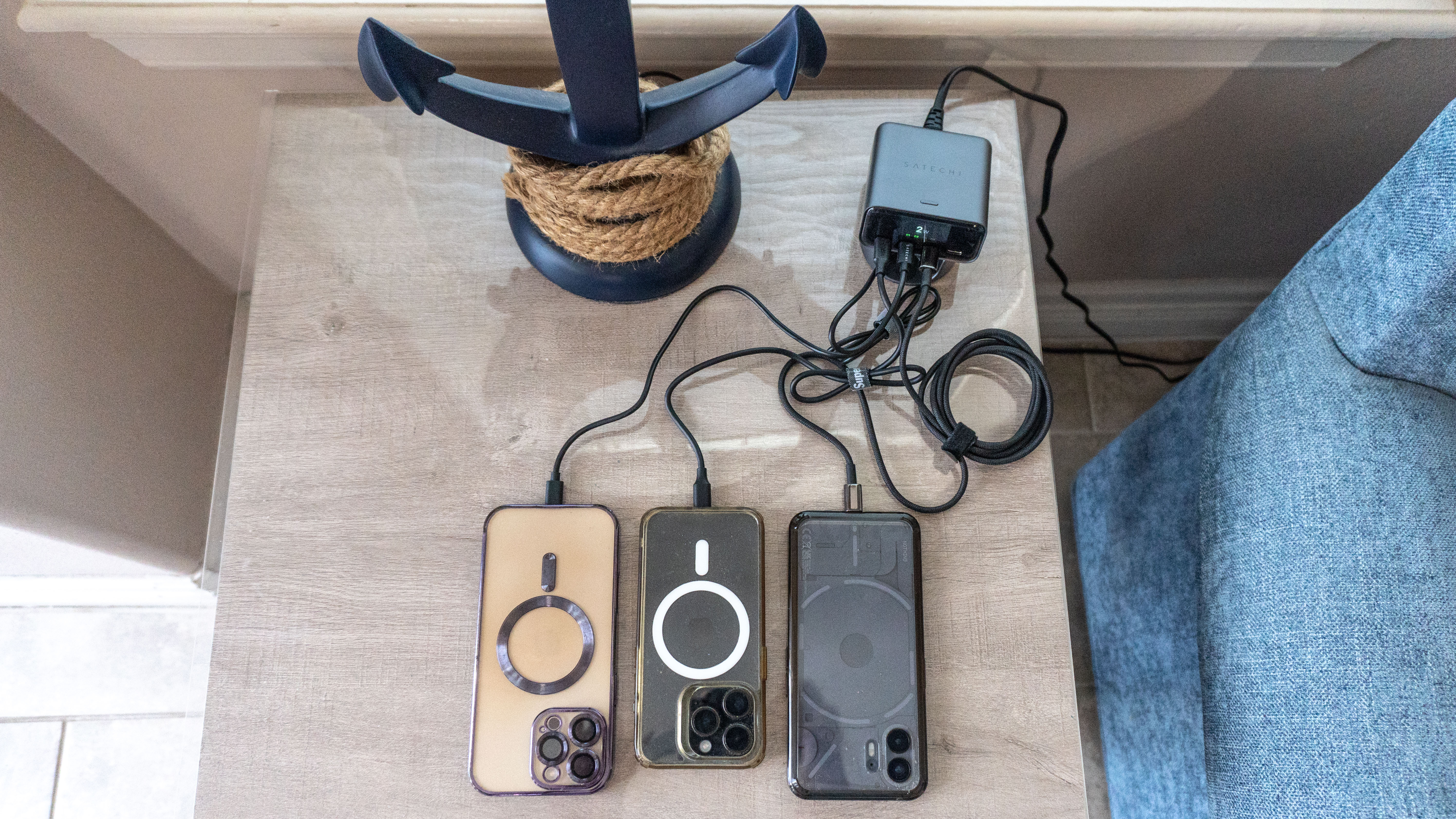 Three phones plugged into the Satechi ChargeView 140W Desktop Charger on an end table next to a couch