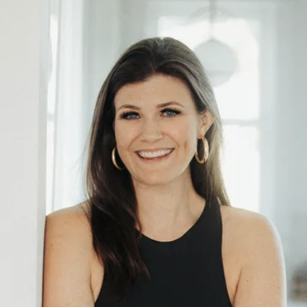 A headshot of a woman with brown hair and hoop earrings smiling at the camera