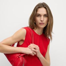 Young woman wearing red mini shift dress and red rectangle handbag with grey background.