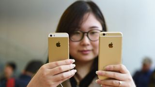 Gold Apple iPhone 5s held against a gold iPhone 6s by a woman in an Apple store