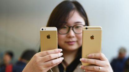 Gold Apple iPhone 5s held against a gold iPhone 6s by a woman in an Apple store
