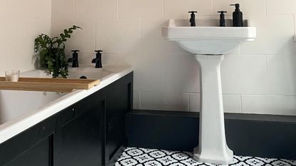bathroom with orange wall, black and white floor tiles and black bath panel, with hanging plant and wall mirror