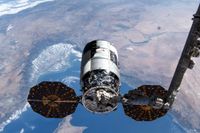 a spacecraft is held by a robotic arm above Earth.