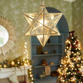 Close up of a star-shaped lamp hanging above a Christmas tree lit up with Christmas lights