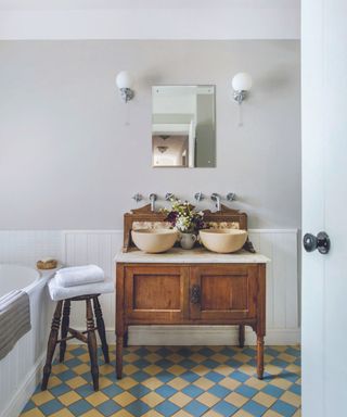 Traditional wooden unit with two round sinks in a bathroom with Victorian floor tiles.