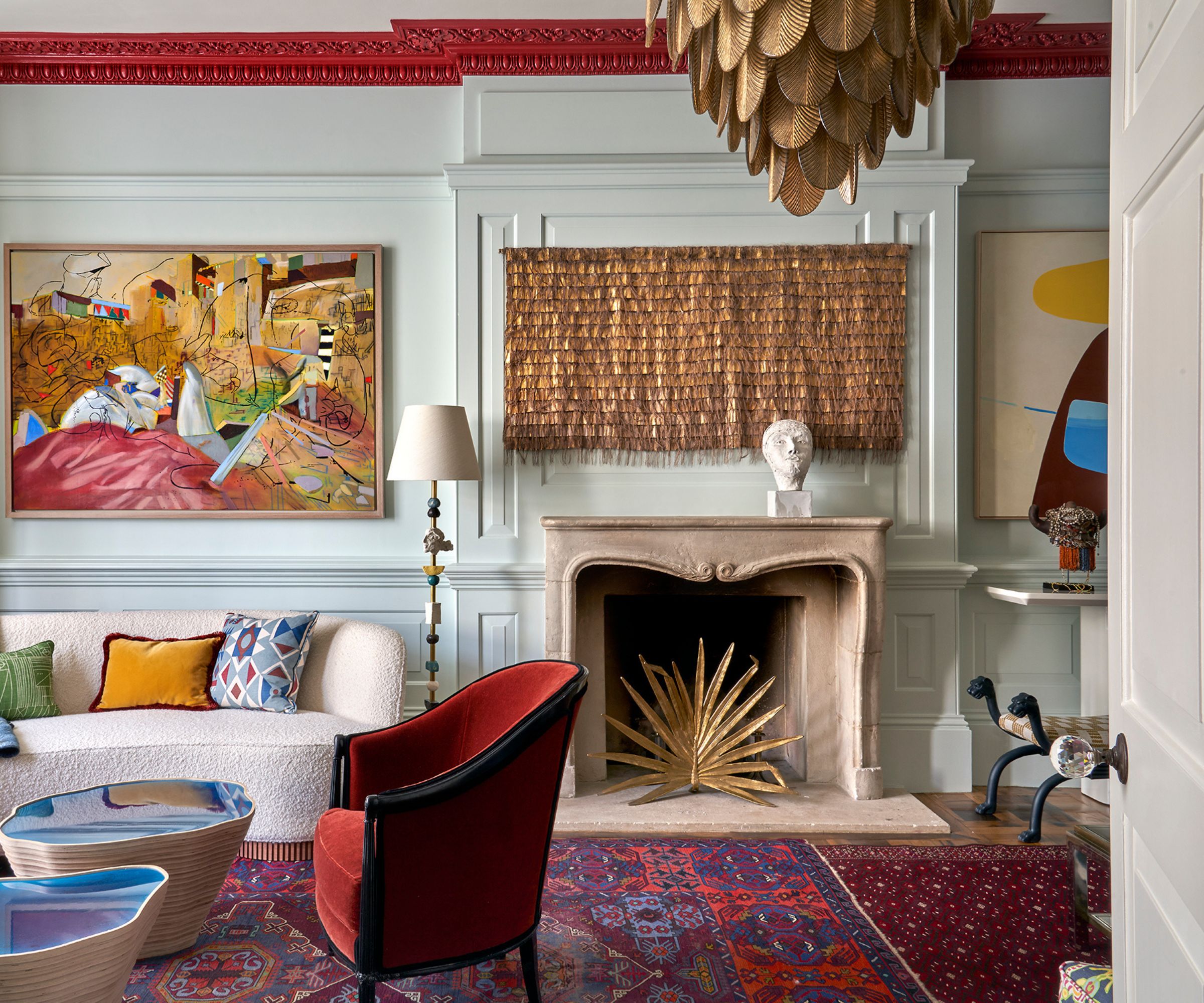 Eclectic living room with a red Persian rug, light blue walls, a marble fireplace, modern art, and a large gold leaf chandelier