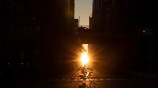 A man rides a bicycle across midtown Manhattan during sunset.