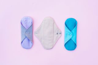 Three reusable sanitary pads are displayed on a lilac background.
