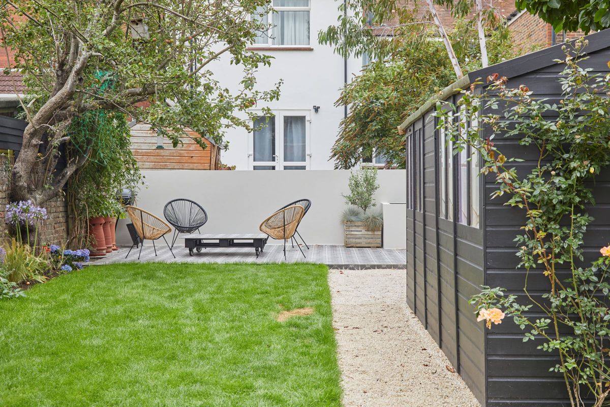 The garden shows a garden shed and white boundary wall with a seating area next to a tree