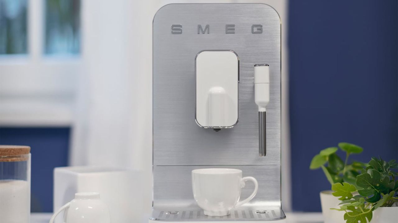 The Smeg BCC02 coffee maker on a countertop with a plant and some coffee cups beside it