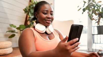 Woman in sports clothes with headphones round her neck looking at phone