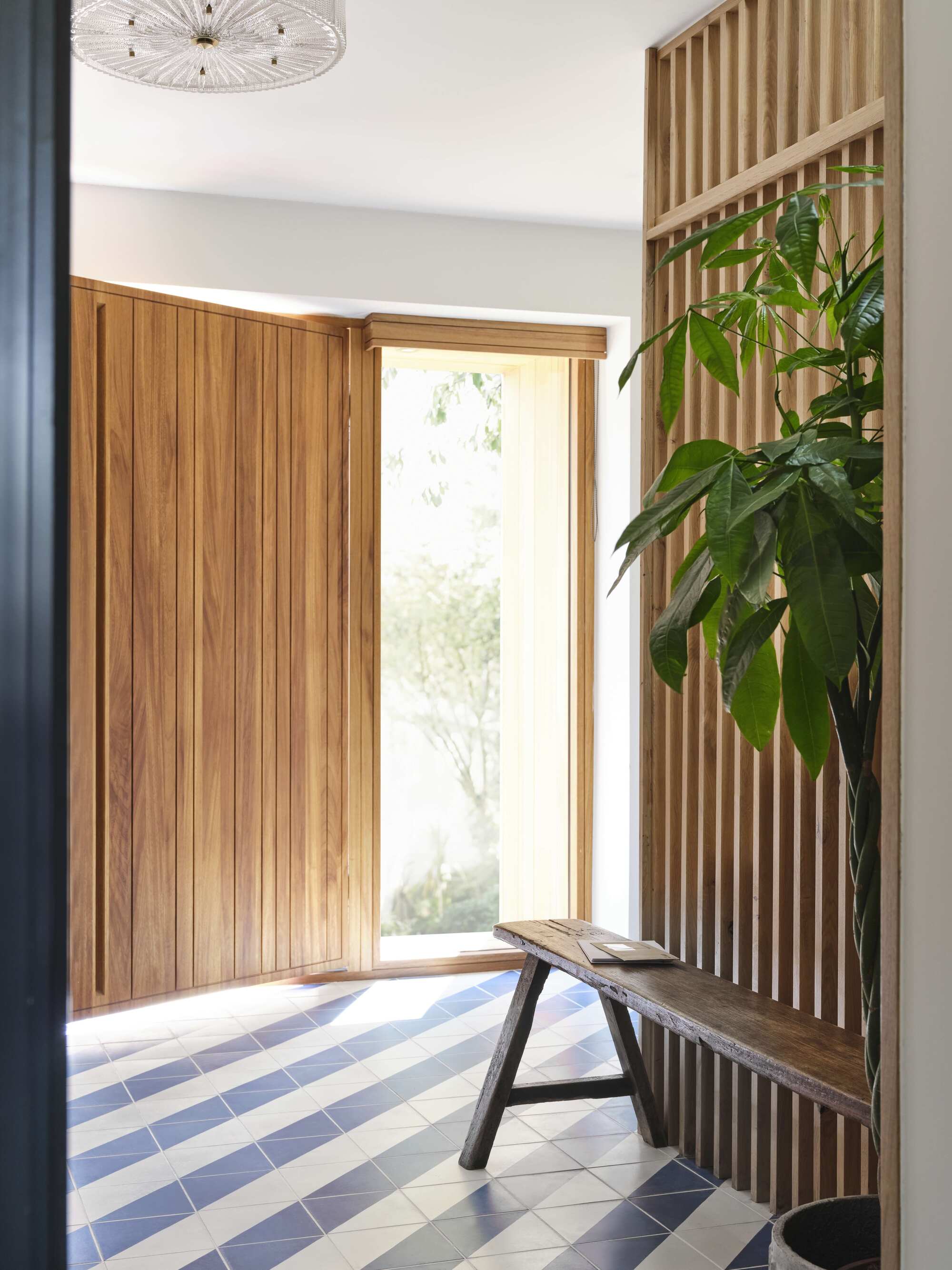 entry hallway with timber door and slatted details, a bench seat, and tall potted plant and blue and white striped floor tiles laid diagonally