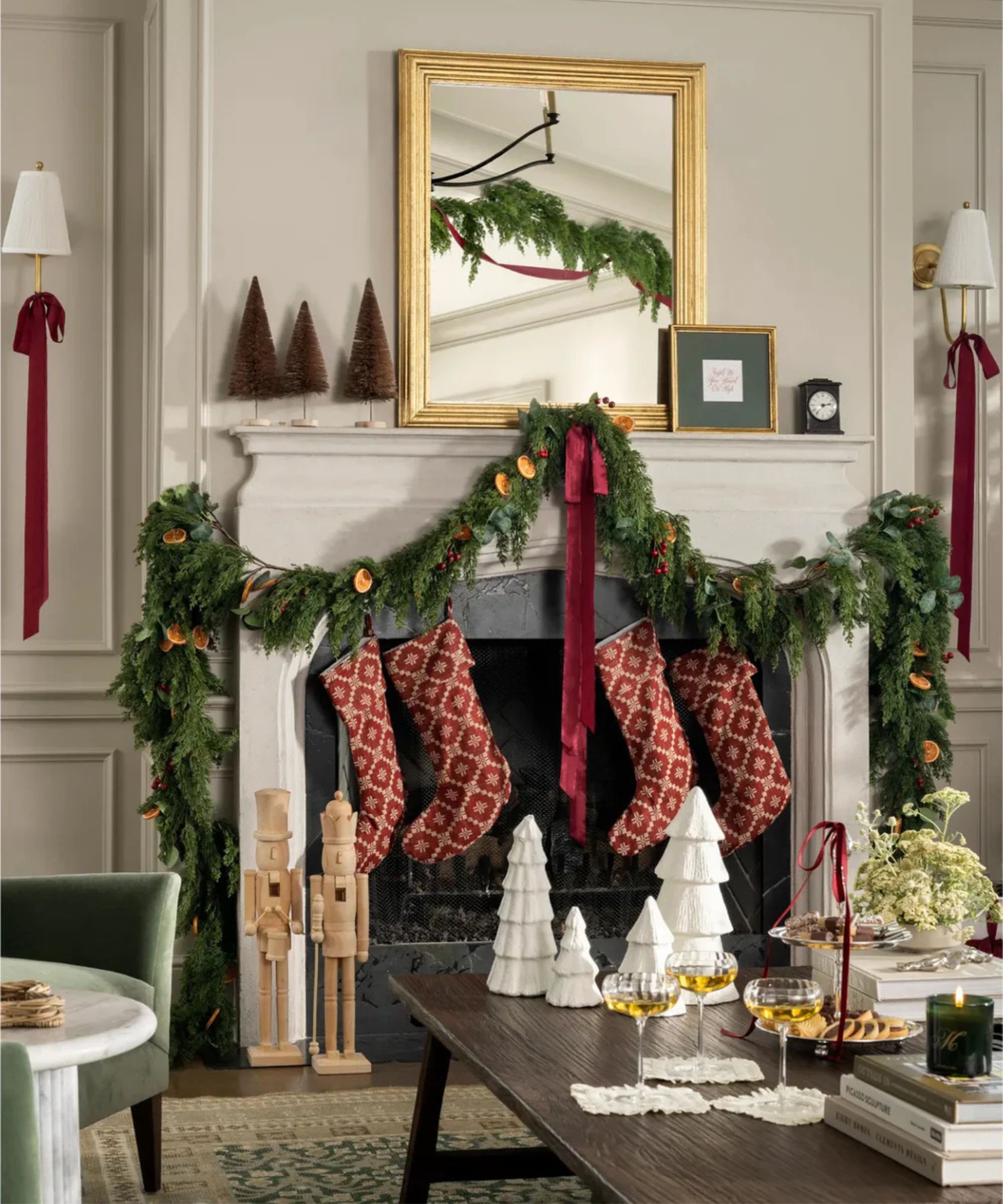 neutral living room with a large fireplace decorated for christmas with a draped garland decorated with dried oranges, red ribbons and red patterned stockings hung