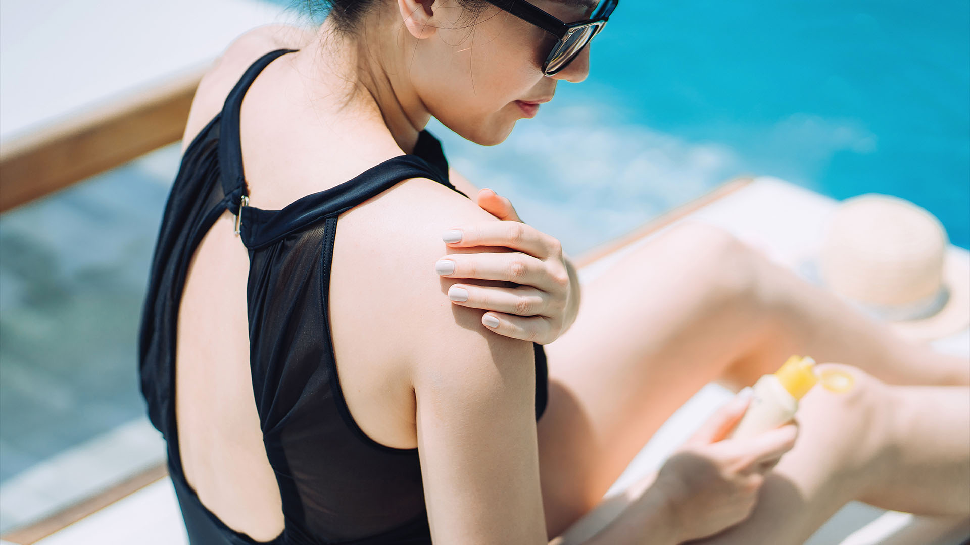 Young woman applying suntan lotion while sunbathing by the swimming pool.