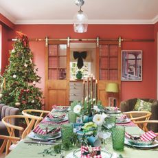 dining room with peach walls and sliding barn doors connecting to kitchen, with table dressed for Christmas and Christmas tree in corner