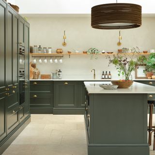 a dark green Shaker kitchen with brass fittings, kitchen island and pale walls