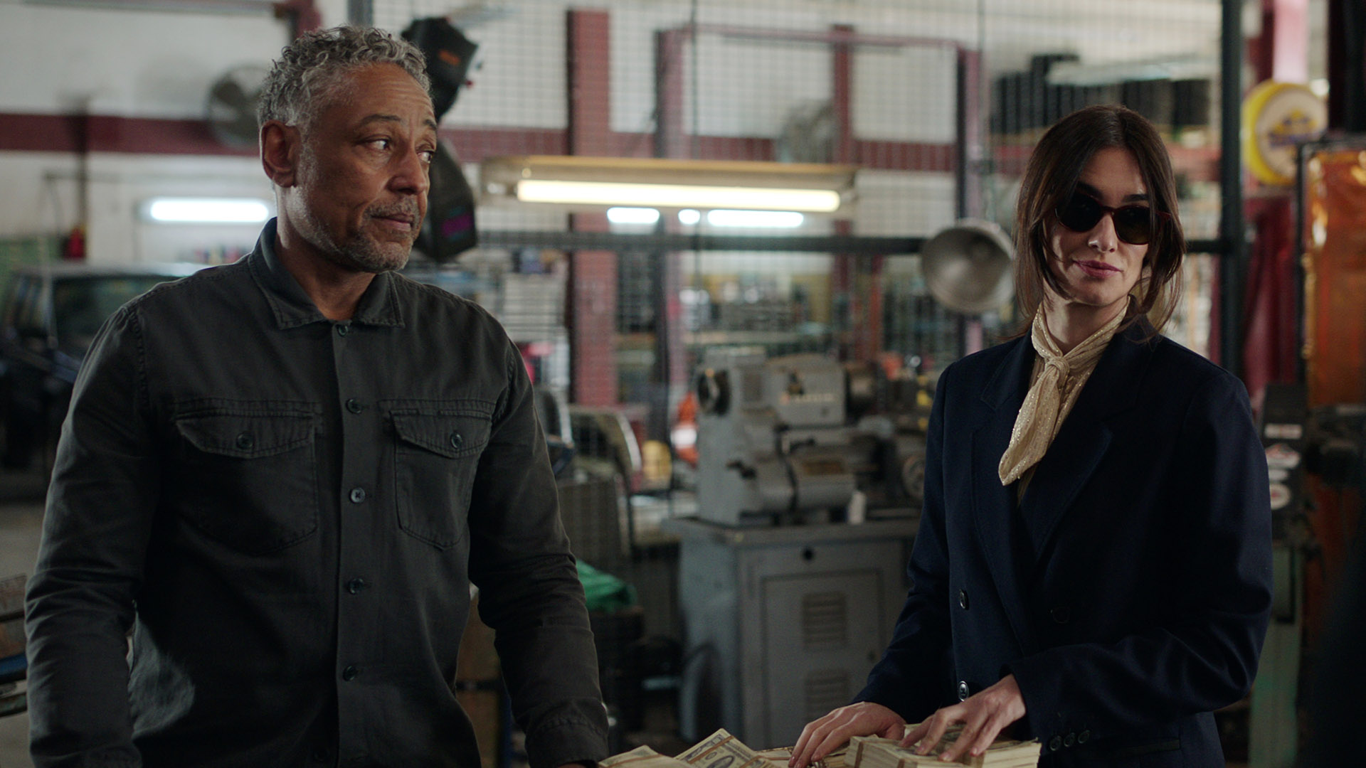 Leo and Ava stand by a table with cash on it in Netflix's Kaleidoscope