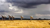 a series of large white radar dishes stand alone in the desert