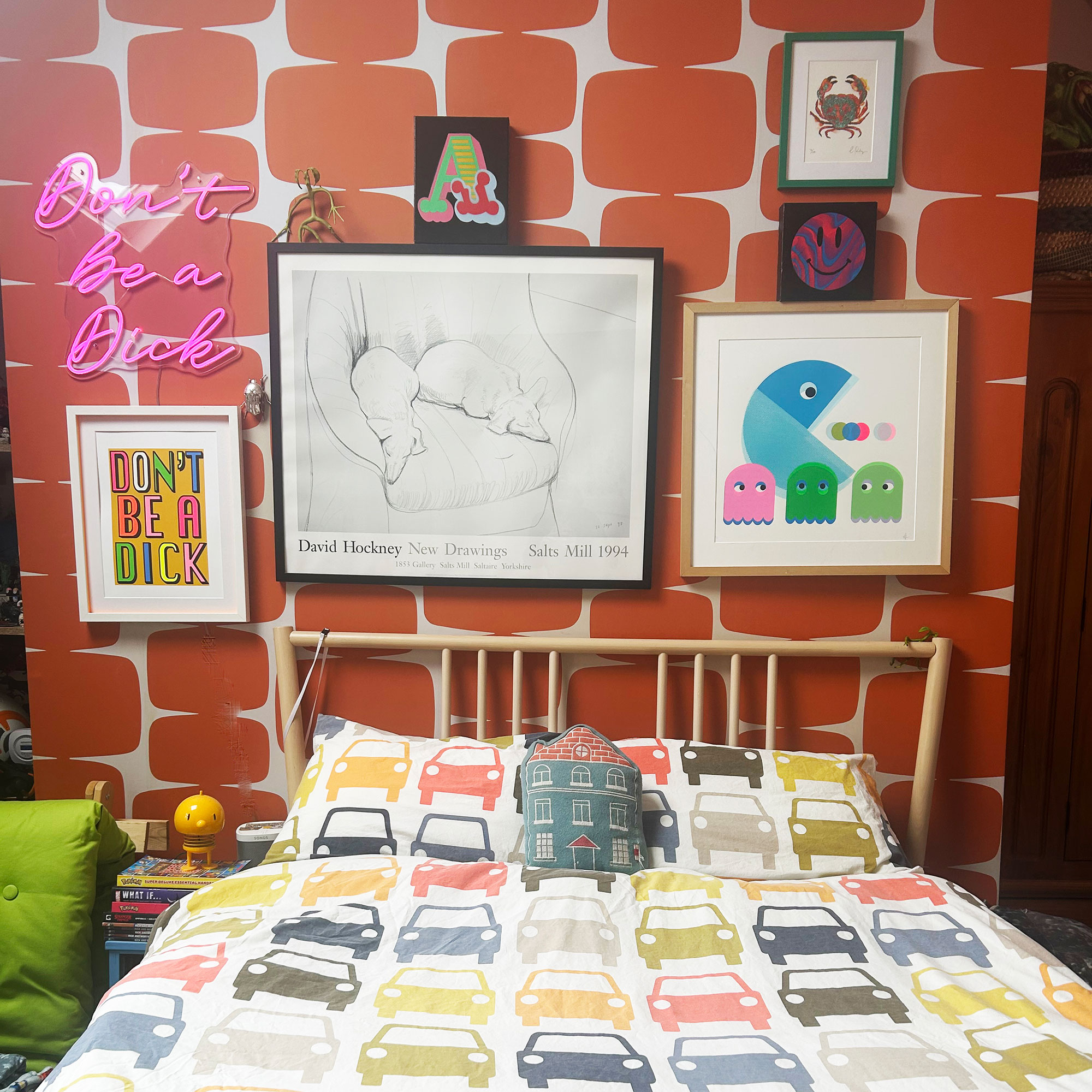 Teenage boy bedroom with orange patterned wallpaper feature wall covered with artwork behind bed