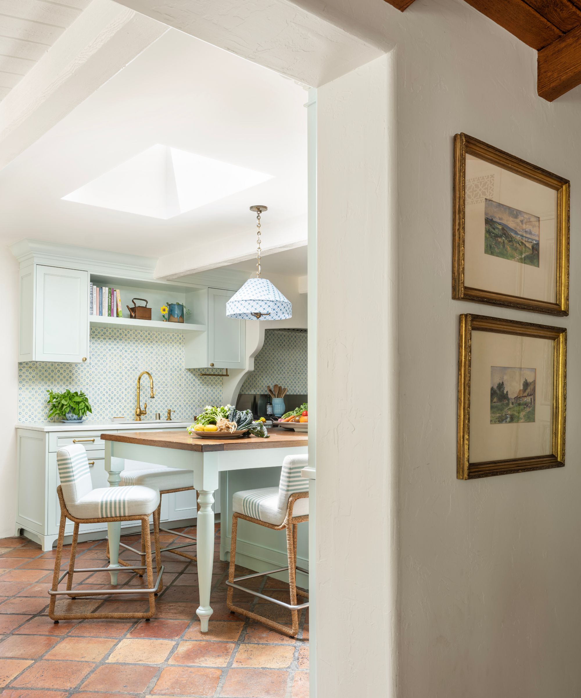A blue/green kitchen with terracotta floor tiles, a tiles backsplash, and a brass faucet