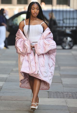 a street style photo of the musician Normani wearing a pink puffer jacker over a white tank top with white shorts and white heels taken at JW Anderson's spring 2025 runway show