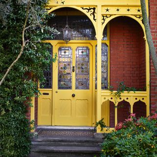 front door colour ideas, yellow front door and porch with ornate Victorian detailing, stained glass windows, steps up to tiled area