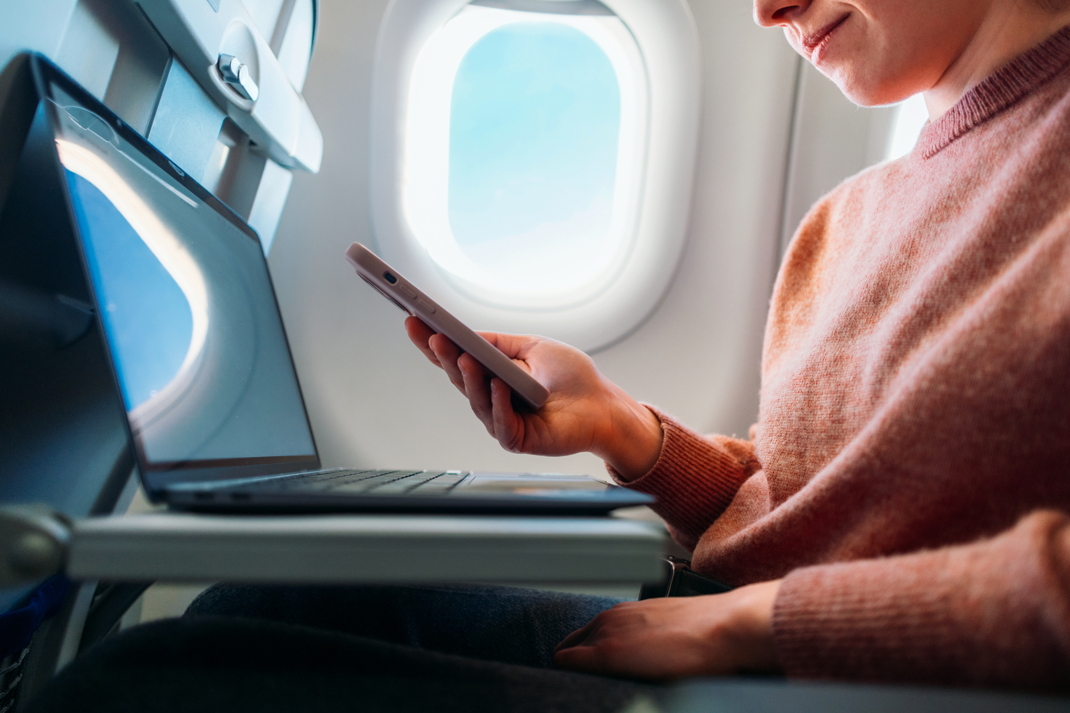 Person looks at phone and laptop as they sit by plane window