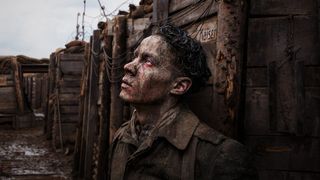 A soldier covered in mud looking up at the sky as he leans against the wall of a trench.