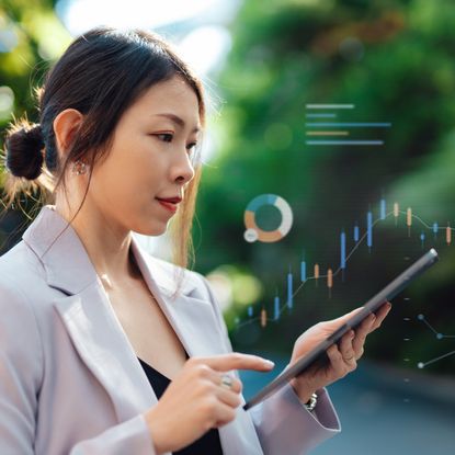 A woman holds a tablet in front of trees. She is surrounded by technological graphics.