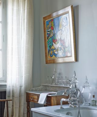 Pale blue bathroom, vintage dressing table, with marble top, bath and mixer taps, colorful antique artwork above sink