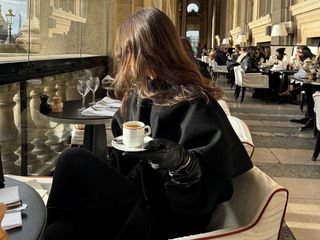 @emmaleger wearing an all black outfit and drinking coffee.