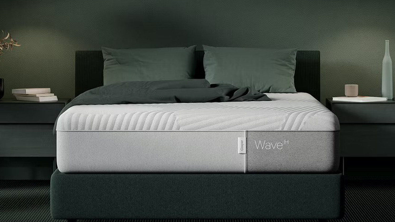 Casper mattress sales, deals and discounts: the Casper Wave Hybrid Mattress shown on a black fabric bed frame in a dark green bedroom