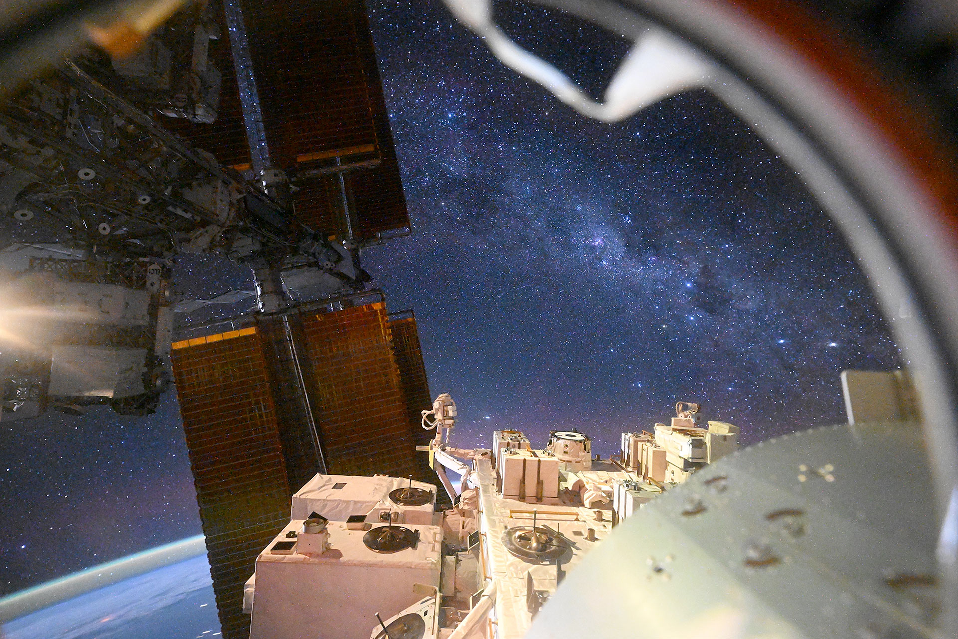 colorful stars and the glow of the galaxy are seen above Earth from a window on a space station