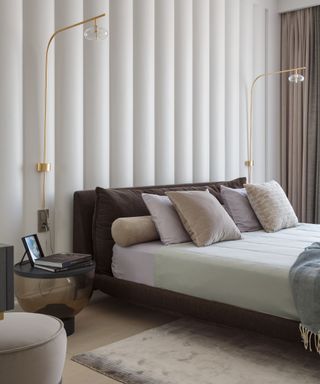 Modern luxury bedroom with large fluted wall design, low bed with velvet neutral cushions and twin tall gold modern lamps and see-through nightstand