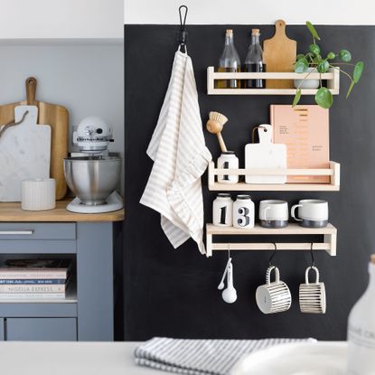 Black wall of kitchen with wooden shelving attached holding kitchen accessories