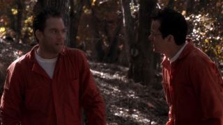 Frank Whaley in a prison uniform, talking to another man in prison uniform, in the woods, in NCIS