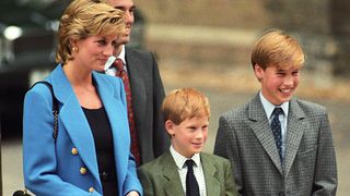 Princess Diana wears a blue suit jacket while posing with young sons Prince Harry and Prince William who wear gray suits during a visit to Eton school