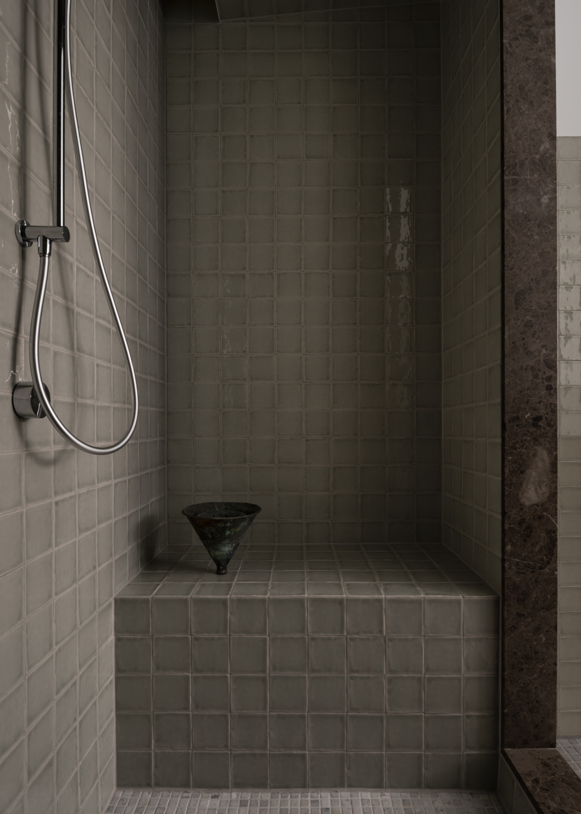 The inside of a steam shower room with gray tiles, a bench, and silver hardware