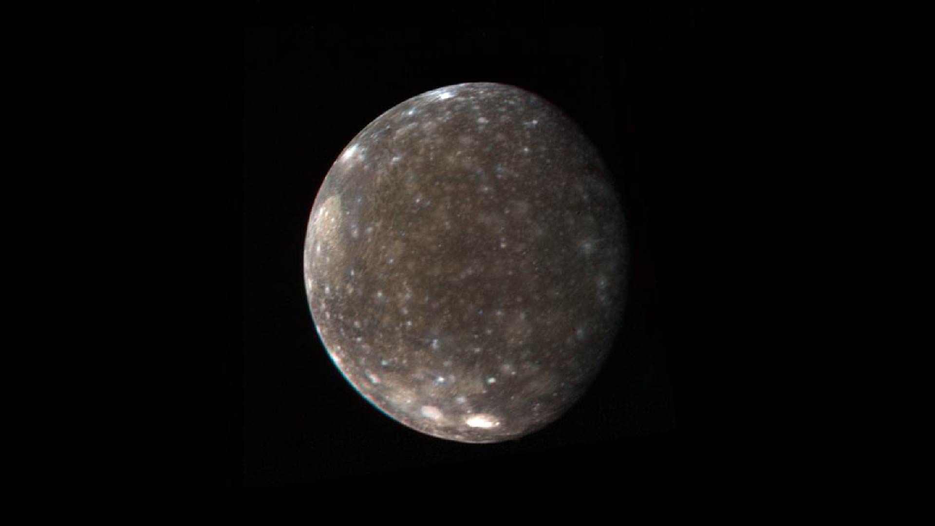An image of Callisto. It is a medium brown with icy blue spots.