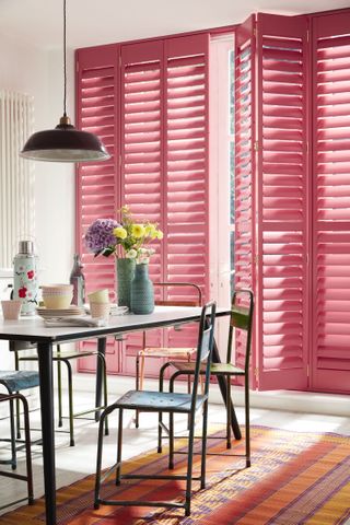 How to design a kitchen: white dining room and kitchen with pink shutters and vibrant rug by the shutter store
