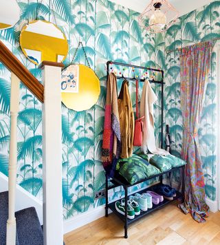 Colourful hallway with green leaf print wallpaper with mirrors hanging next to stair case