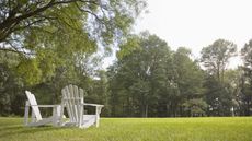 A pair of white chairs sits looking out over a green lawn in the summer