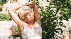 Woman stretches outside with the sun on her face. Her eyes are closed and she looks contented